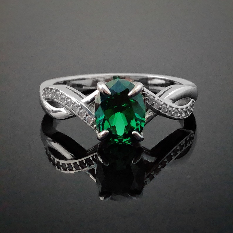 Puede incluir: Un anillo de plata con una piedra ovalada verde y piedras m&aacute;s peque&ntilde;as transparentes engastadas en una banda retorcida.
