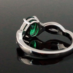 Puede incluir: Un anillo de plata con una piedra preciosa verde engastada en garras. El anillo tiene una banda delicada con un dise&ntilde;o curvo.