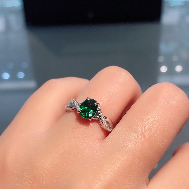 Puede incluir: Un anillo de plata con una piedra preciosa verde y peque&ntilde;as piedras transparentes engastadas en una banda retorcida.