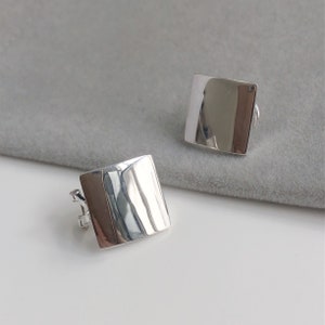 May include: A pair of silver square earrings. The earrings are smooth and have a slightly textured surface.