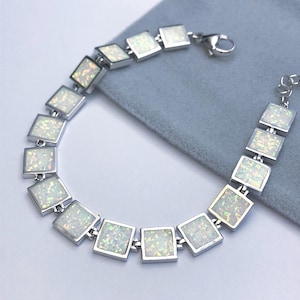 May include: A silver bracelet featuring square-shaped opal stones. The stones are iridescent and display a white, blue, and green colour.