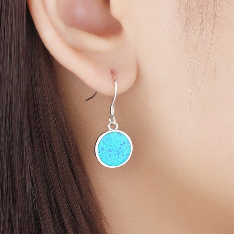 May include: A silver earring with a round, turquoise-colored stone. The earring is a simple drop style, with a hook that goes through the ear. The stone has a speckled appearance, and the metal is shiny.