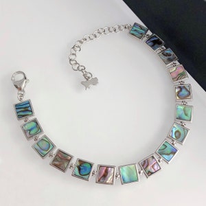 May include: A silver bracelet with a chain and square-shaped abalone shell charms. The charms have iridescent green, blue, and purple colors.