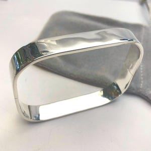 May include: A silver bangle bracelet with a square shape and a polished finish.