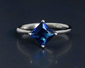 May include: A silver ring with a square-shaped blue gemstone.