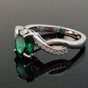 Puede incluir: Un anillo de plata con una gran piedra preciosa verde esmeralda y piedras preciosas transparentes m&aacute;s peque&ntilde;as engastadas en una banda retorcida.