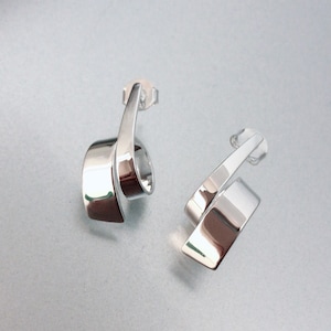May include: A pair of polished silver earrings. Each earring has a curved, ribbon-like design with a post backing. The earrings have a reflective surface, catching the light and creating a bright, modern look.