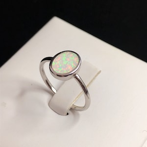 Könnte beinhalten: Ein silberner Ring mit einem weißen ovalen Opal-Edelstein. Der Opal hat einen grün-rosa schillernden Glanz.
