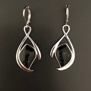 May include: A pair of silver dangle earrings with black gemstone accents. The earrings feature a unique, abstract design with a teardrop shape.
