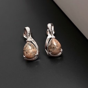 May include: A pair of silver earrings with a teardrop-shaped stone. The stones are a light brown color with a speckled pattern.