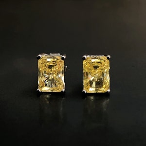 May include: A pair of silver stud earrings with yellow square-shaped cubic zirconia stones.
