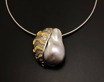 May include: A silver chain necklace with a pendant featuring a large, pearlescent white baroque pearl set in a gold and silver patterned frame.
