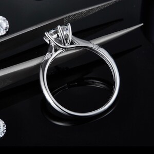 May include: A silver engagement ring with a large, round, clear center stone and smaller, clear stones on the band.