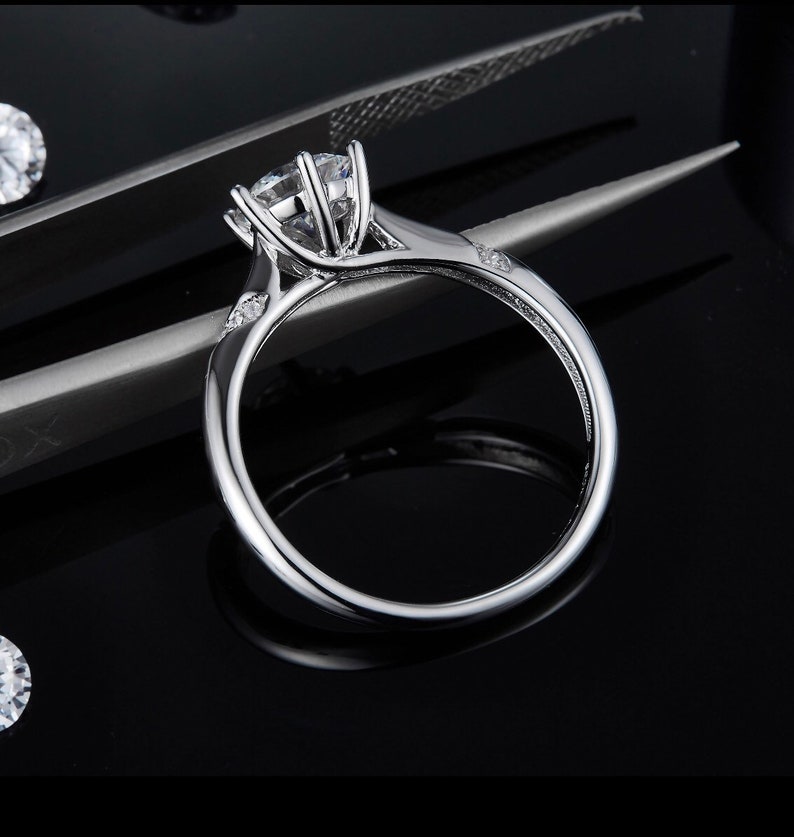 May include: A silver engagement ring with a large, round, clear center stone and smaller, clear stones on the band.