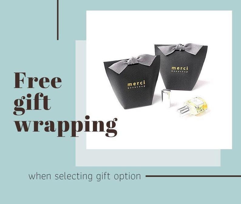 May include: Two black gift boxes with gray bows, each bearing the gold text "merci beaucoup." A perfume bottle is next to the boxes. The words "Free gift wrapping" are displayed in the image.