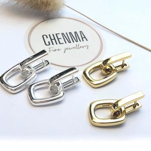 May include: Two pairs of square-shaped earrings, one pair is silver and the other is gold. The earrings have a simple design with a small loop in the center. The earrings are displayed on a white surface with a logo that says "Chenna Fine Jewellery".