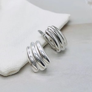 May include: A pair of silver hoop earrings with a unique, multi-layered design. The earrings are made of smooth, rounded metal and have a polished finish.