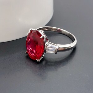 Puede incluir: Un anillo de plata con una gran piedra de rubí ovalada y dos pequeños acentos de diamantes.