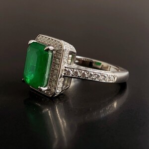 May include: A silver ring with a large emerald green gemstone surrounded by smaller clear gemstones.