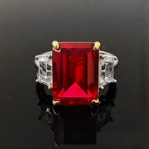 Könnte beinhalten: Ein silberner Ring mit einem großen, rechteckigen, roten Edelstein, der von zwei kleineren, klaren Edelsteinen umgeben ist.