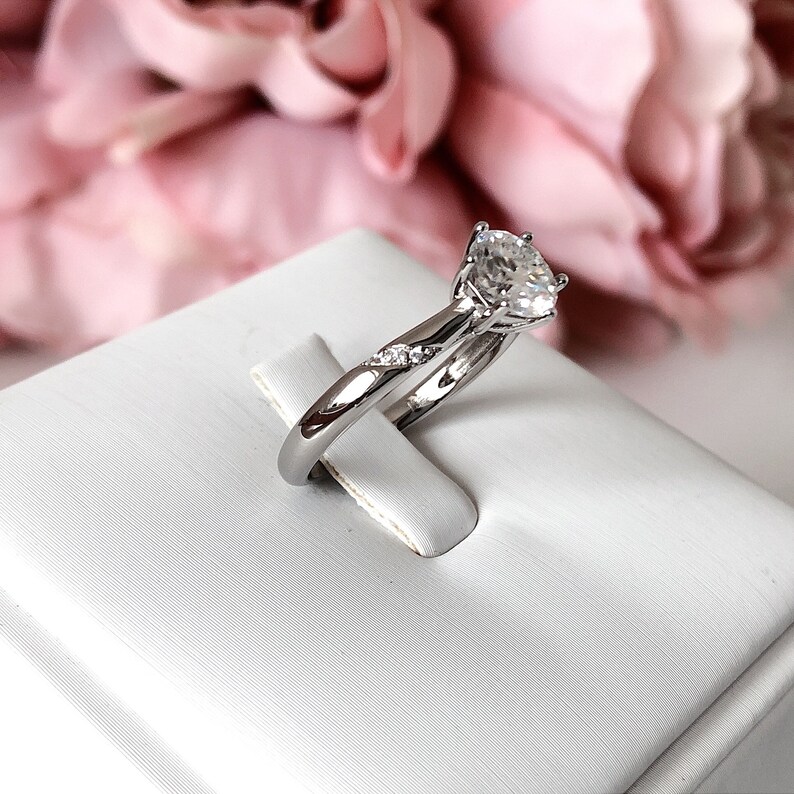 May include: A silver engagement ring with a large, clear, round-cut diamond in the center. The band is accented with smaller diamonds.