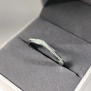 Könnte beinhalten: Ein silberner Bandring mit einem weißen Opal-Inlay. Der Ring ist in einem V-förmigen Design gesetzt.