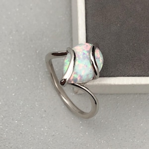 May include: A silver ring featuring a white opal gemstone set in a delicate, curved design.