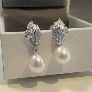 May include: A pair of silver earrings with a leaf design and a white pearl drop.