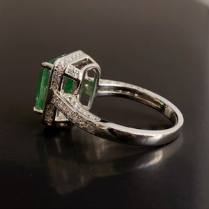 May include: A silver ring with a large emerald green gemstone surrounded by smaller clear gemstones.
