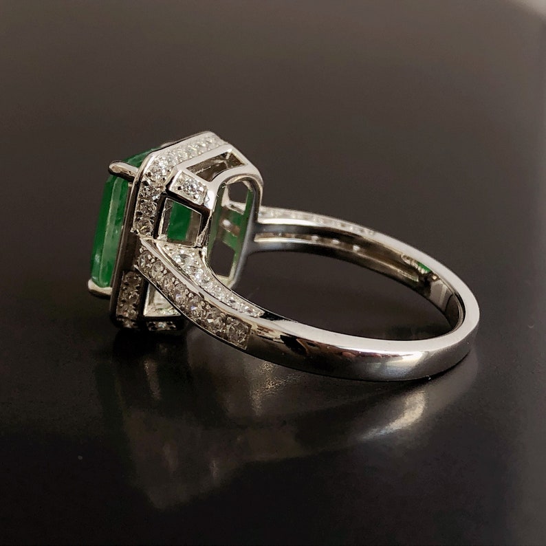 May include: A silver ring with a large emerald green gemstone surrounded by smaller clear gemstones.