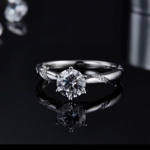 May include: A silver engagement ring with a large, round, clear diamond center stone. The band is twisted and features smaller diamonds on the sides.