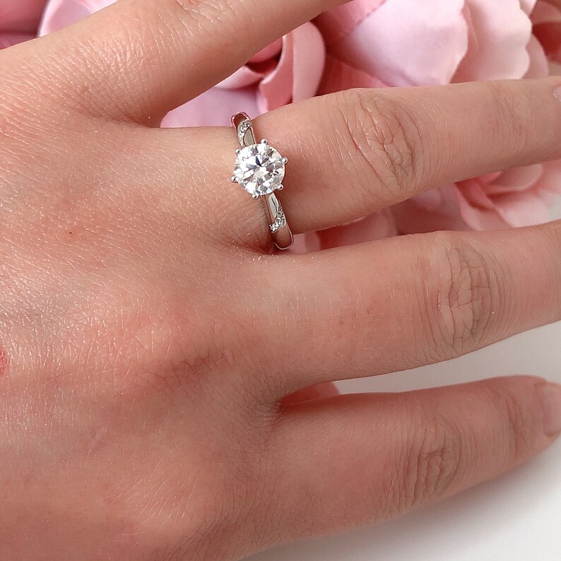 May include: A silver engagement ring with a round, clear diamond center stone and smaller diamonds set in the band.