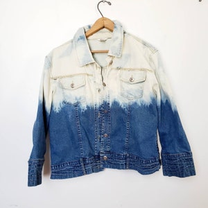 May include: A denim jacket with a white ombre effect. The jacket has a button closure, two chest pockets, and long sleeves.