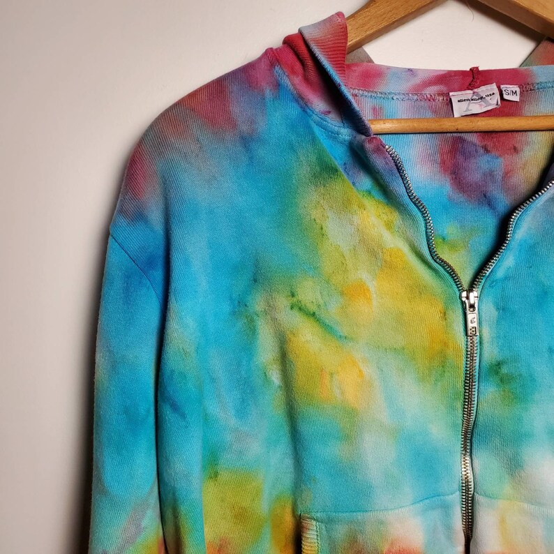 May include: A tie-dye zip-up hoodie with a blue, yellow, red, and green color scheme. The hoodie has a zipper closure and a hood. The tag on the hoodie reads "Made in Vietnam" and "SM".