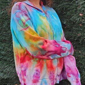 May include: A tie-dye zip-up hoodie with a rainbow color pattern. The hoodie has a hood and a front pocket.