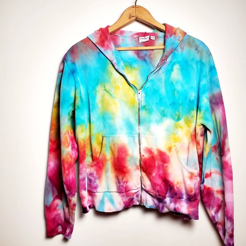 May include: A tie-dye zip-up hoodie with a bright blue, yellow, pink, and purple color scheme. The hoodie has a hood and two pockets.
