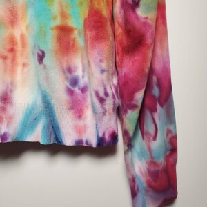 May include: A tie-dye sweater with a colorful pattern of pink, blue, green, and orange. The sweater has long sleeves and a ribbed knit texture.