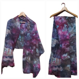 K&ouml;nnte beinhalten: Ein lila, rosa und blauer Seidenschal mit einem Batik-Muster. Der Schal ist gefaltet und &uuml;ber einen Holzb&uuml;gel gelegt.