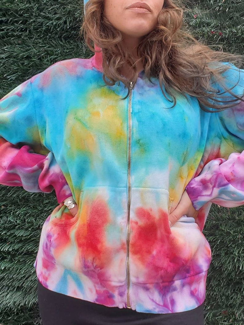 May include: A tie-dye zip-up hoodie with a blue, pink, yellow, and white color scheme. The hoodie has a front pocket and a zipper closure.