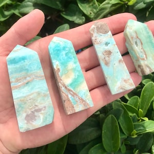 May include: Four aqua blue and brown agate crystal points with a pointed top and a flat base. The points are arranged in a row on a hand.