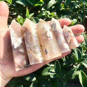 Puede incluir: Cinco puntas de cristal de ágata en varios tonos de blanco, rosa y marrón con inclusiones blancas y marrones. Las puntas están dispuestas en fila, con la punta más grande en la parte posterior y la punta más pequeña en la parte delantera.