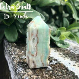 May include: A green and brown crystal point, also known as a tower, with a pointed top and a flat base. The crystal is approximately 1.5 to 2 inches tall. Extra Small.