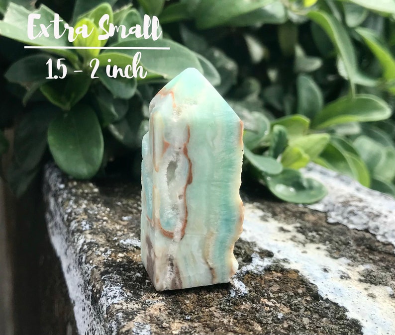 May include: A green and brown crystal point, also known as a tower, with a pointed top and a flat base. The crystal is approximately 1.5 to 2 inches tall. Extra Small.