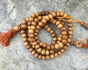 Puede incluir: Un collar de cuentas mala de madera marrón con un borla en cada extremo. Las cuentas son redondas y tienen un acabado liso. El collar está enhebrado en un cordón delgado.