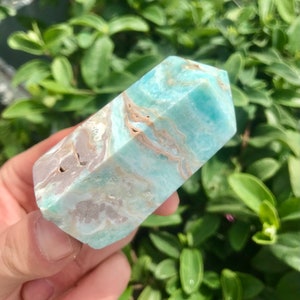 May include: A light blue and brown, polished,  faceted,  crystal point. The crystal has a natural,  rough,  textured surface.