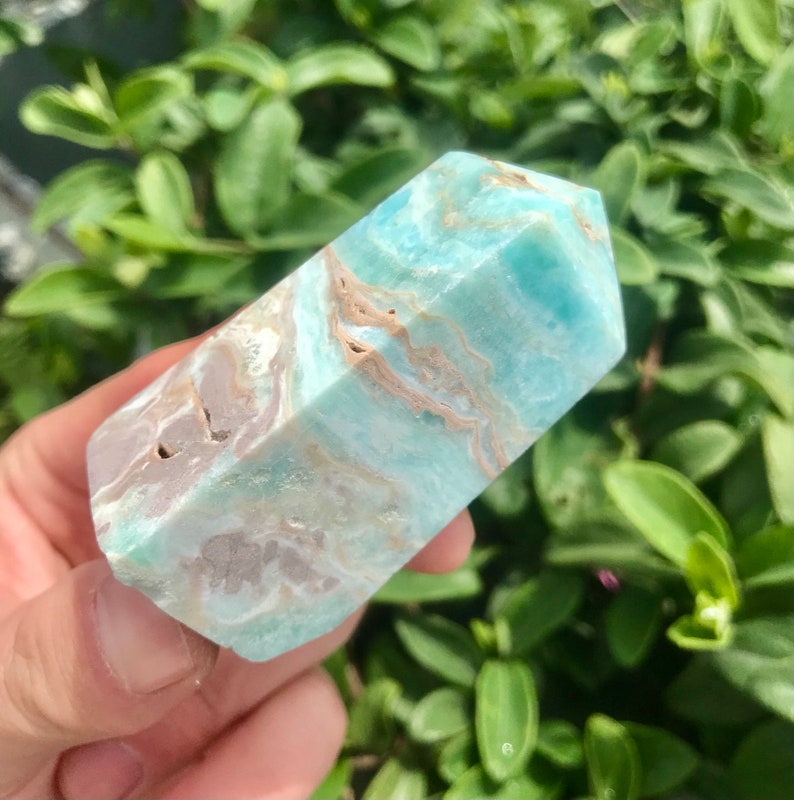 May include: A light blue and brown, polished,  faceted,  crystal point. The crystal has a natural,  rough,  textured surface.