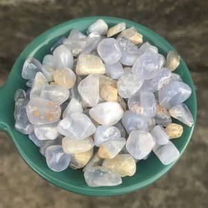 Puede incluir: Un bol lleno de piedras de &aacute;gata azul lazada pulidas. Las piedras son de color azul claro con marcas blancas y marrones.