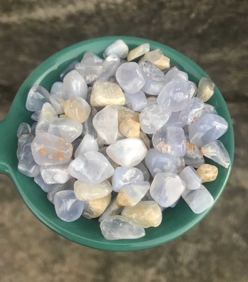 Puede incluir: Un bol lleno de piedras de &aacute;gata azul lazada pulidas. Las piedras son de color azul claro con marcas blancas y marrones.