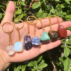 May include: Seven different gemstone keychains with gold chains and rings. The gemstones are amethyst, blue sodalite, opal, clear quartz, aventurine, tiger's eye, and red jasper.