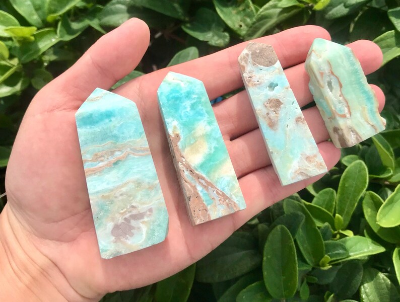 May include: Four aqua blue and brown agate crystal points with a pointed top and a flat base. The points are arranged in a row on a hand.